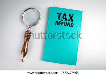 Tax Refund. Green book cover and magnifying glass on a gray table