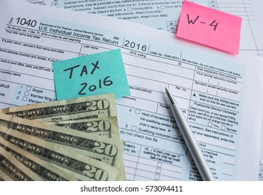 Tax time 2016 and W - 4 written on a bright stickers for a tax form 1040 with pen and twenty dollars banknotes