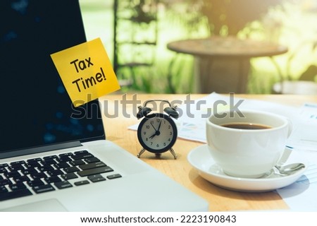 Tax time Concept. tax time post-it on a laptop and clock, a cup of coffee, and an Individual income tax return form . income tax online