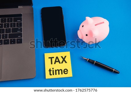 Tax time - notification of the need to file tax returns, tax form at accauntant workplace. Piggy bank in pink color with laptop and smartphone on blue background