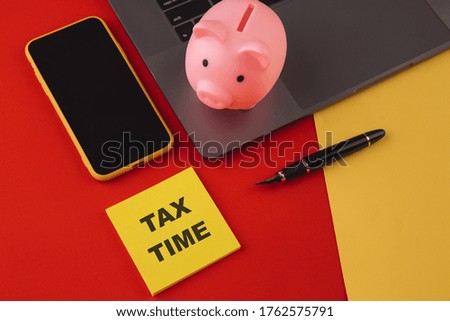 Tax time - notification of the need to file tax returns, tax form at accauntant workplace. Piggy bank in pink color with laptop, pen and smartphone on colorful background