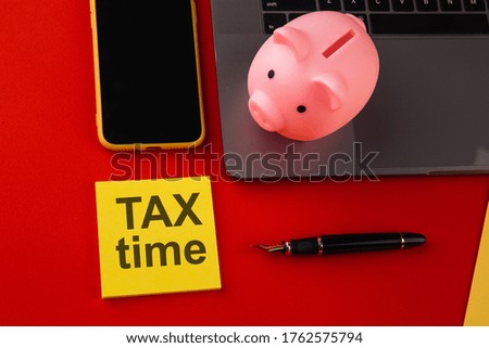Tax time - notification of the need to file tax returns, tax form at accauntant workplace. Piggy bank in pink color with laptop and smartphone on colorful background