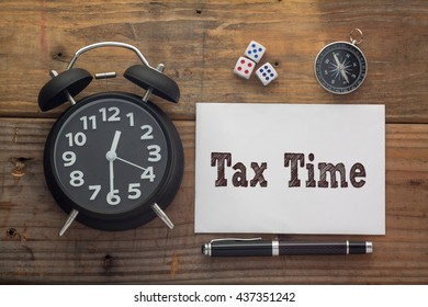 Tax Time Written On Paper With Wooden Background Desk,clock,dice,compass And Pen.Top View Conceptual