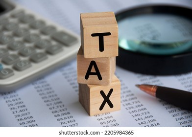 Tax Word On Wooden Blocks With Calculator, Pen, Magnifying Glass And Data Analysis Background. Tax Concept.