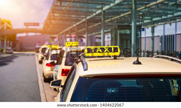 Taxi\
cabs waiting for passengers. Yellow taxi sign on cab cars. Taxi\
cars waiting arrival passengers in front of Airport Gate. Taxis\
stand on Airport Terminal waiting for\
passengers.