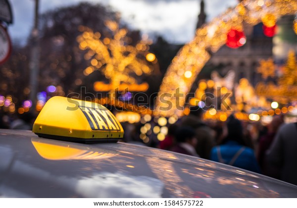 Taxi car at city\
street near Christmas market in Rathausplatz, Vienna, Austria.\
Close-up yellow taxi sign on car rooftop at night. Public\
transportation in downtown\
district