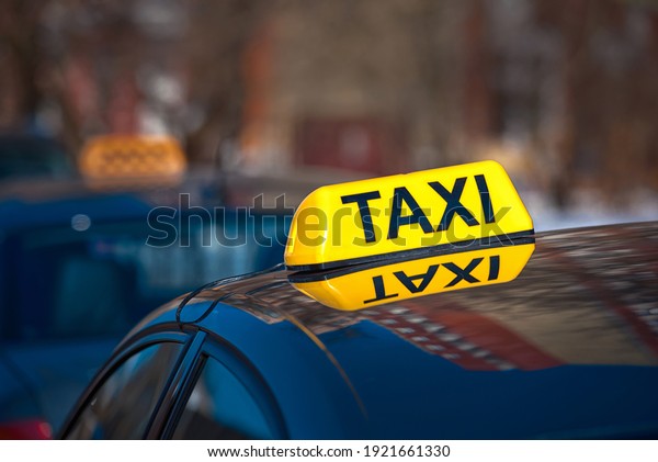 Taxi car sign at day\
time, taxi sign on cab roof while parking on road waiting for\
passaenger. Taxi rank. Taking safe rideshare during coronavirus.\
Luminous taxi top sign