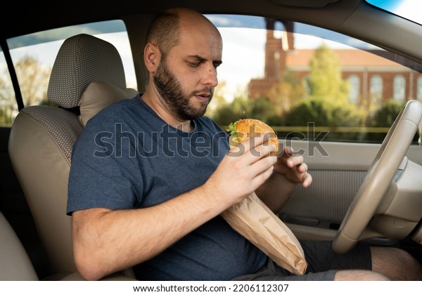 Taxi driver eating burger\
in the car as the traffic is very bad in the morning. eat hamburger\
in car