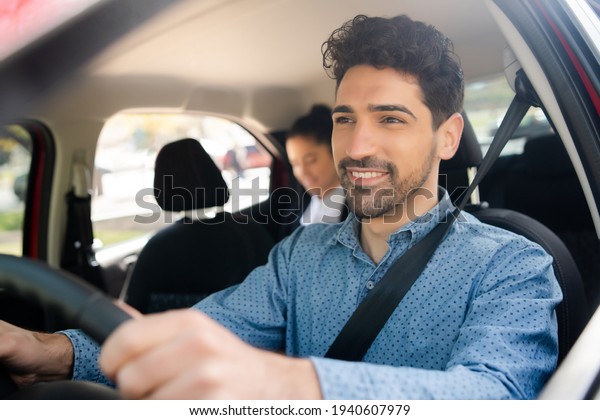 Taxi driver with\
passenger at back seat.