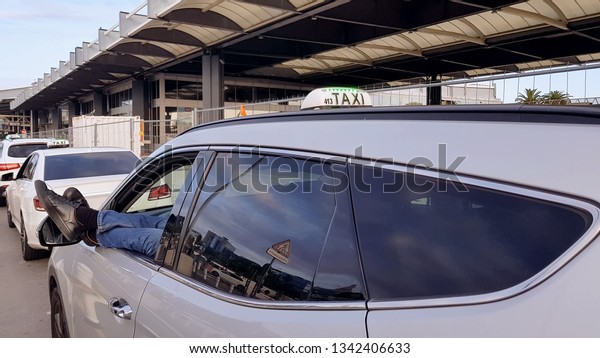 Taxi driver resting car airport parking,\
legs outside, passenger\
transportation