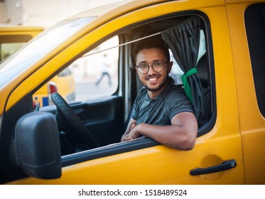 The taxi driver smiles happily, sitting in the cab of a yellow car