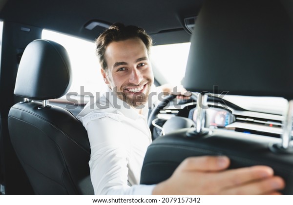 Taxi driver\
smiling while turning over to the backseat looking talking with\
clients. Successful businessman husband looking at the backseat at\
dealer shop before buying a\
car