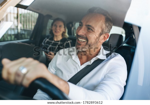 Taxi driver\
talking to a female passenger sitting in backseat. Businesswoman\
using taxi ride to go to\
work.