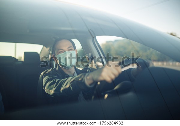 Taxi\
driver wearing sterile medical mask hold his hands on the steering\
wheel. Young man drives a car with a passenger during coronavirus\
epidemic. Social distance, pandemic, health\
concept.
