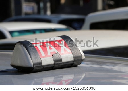 Taxi light sign or cab sign in white and red color with white text and tied with black tape on the car roof at the street blurred background, Myanmar.