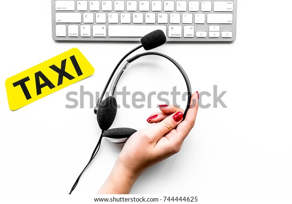 Taxi service\
online. Women hand hold headphones near taxi label, keyboard on\
white background top view