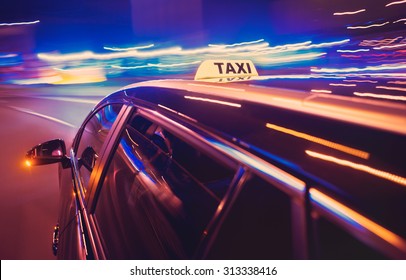 Taxi taking a left turn at night in an urban surrounding, seen from the rear end of the cab