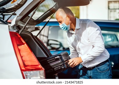 A Taxi Or Uber Driver In Mask Puts The Luggage Into The Trunk Of His Car