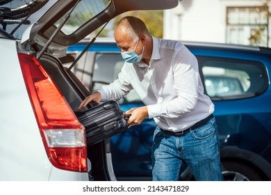 A Taxi Or Uber Driver In Mask Puts The Luggage Into The Trunk Of His Car