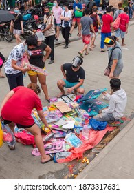 Taytay, Rizal, Philippines - Dec 2020: A Vendor Sells Cheap Toys By The Sidewalk. A Few Interested Customers Check For The Best Ones. They Are Wearing Face Masks And Shields.