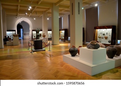 Tbilisi, Georgia - May 19, 2018: Inside An Exhibit Hall Room Of The Georgian National Museum Where Ancient Artefacts Including Pottery Are Displayed. Two Museum Employees Are Seated Near The Entrance.