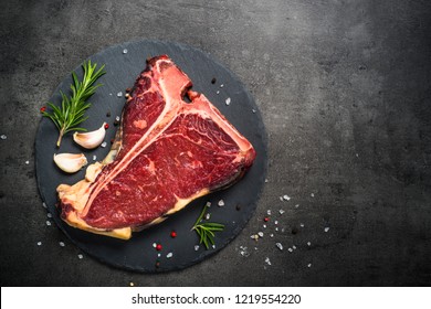 T-bone beef steak on black background with spices. Ready for cooking. Top view with copy space.
