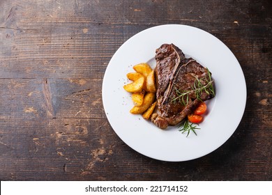 T-Bone Steak with roasted potato wedges on white plate on wooden background - Powered by Shutterstock