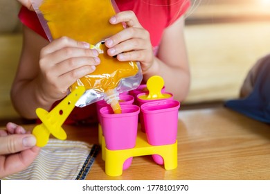 TCute Adorable Young Caucasian Little Girl Kid Sitting At Table Home Yard And Have Fun Making With Mom Homemade Fruit Puree Icecream. Young Happy Child Enjoy Cooking With Mother Outside. Family Love