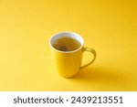 Tea bag in a yellow mug on a yellow background.