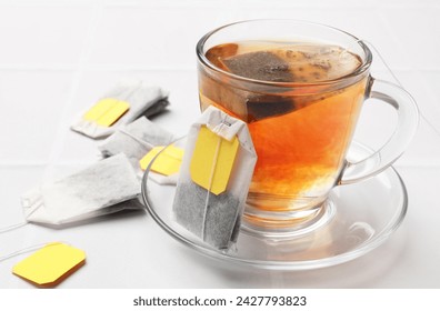 Tea bags and cup of aromatic drink on white table, closeup. Space for text
