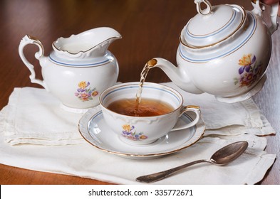 Tea being poured into cup, tea set on wood