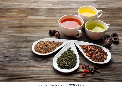 Tea Concept. Different Kinds Of Dry Tea In Ceramic Bowls And Cups Of Aromatic Tea On Wooden Background