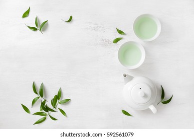 Tea concept, two white cups of tea and teapot surrounded with green tea leaves, view from above, space for a text