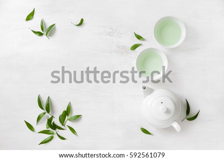 Tea concept, two white cups of tea and teapot surrounded with green tea leaves, view from above, space for a text