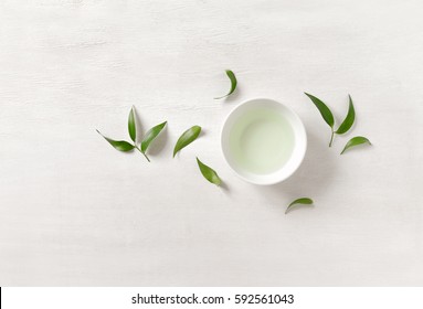 Tea Concept, White Cup With Tea Surrounded With Green Tea Leaves, View From Above