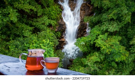 Tea In Jug And Glass On The Bacony And Beautiful Waterfall And Green Leaves Forest Blur Background, Healthy Indulge In The Nature Concept,