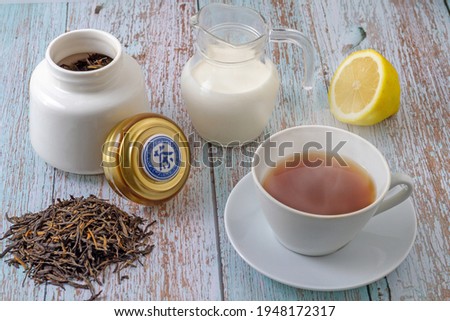 Tea leaves ready for infusion, white cup with tea infusion, lemon cut in half, jug with milk and white bottle containing tea inside. The lid that rests on the pot has the word tea written in Chinese.