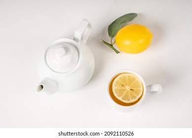 Tea With Lemon, Fresh Healthy Tea, Antioxidant Detox Lemonade, Green Leafy Lemon Next To White Porcelain Teapot On White Isolate Background, A Cup Full Of Tea With Sliced Lemon