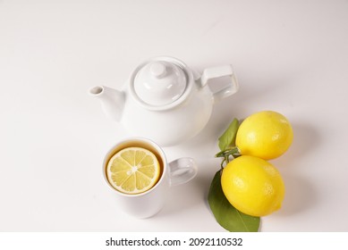 Tea With Lemon, Fresh Healthy Tea, Antioxidant Detox Lemonade, Green Leafy Lemon Next To White Porcelain Teapot On White Isolate Background, A Cup Full Of Tea With Sliced Lemon