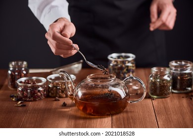 Tea Master Adding A Spoon Of Leaves Into A Glass Pot With Hot Water. Man Brewing High Class Black Tea For Customers.