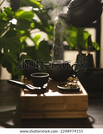 Tea master pouring tea from teapot in sunlight with steam. Tea ceremony. Process of brewing Chinese tea the original method with tools on table and green leaves. Copy space, selective focus.