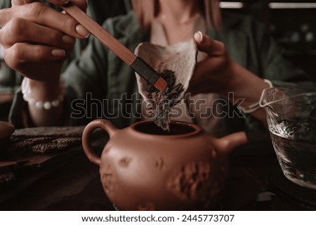 A tea master prepares for a tea ceremony. The setting is serene with multiple teapots in the foreground and a person in traditional attire in the background