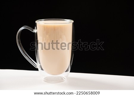 Tea with milk in a glass cup with a double bottom on a white and black background