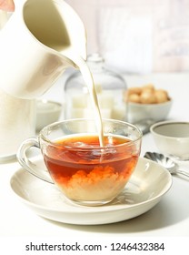 Tea With Milk. Photo With The Cup. White Background. The Cup Is Transparent. The Time Of Adding Milk To Tea.