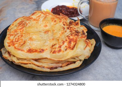 Tea with milk, Roti canai or Roti Parata and curry sauce on the plate over wooden  table