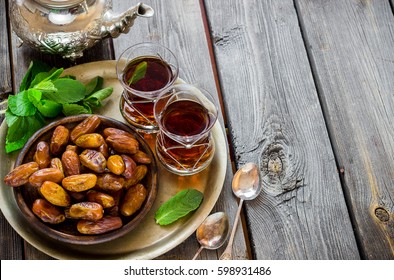 Tea with mint in arab style and dates on wooden table. Selective focus.