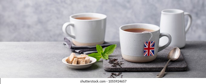 Tea in mugs with British flag tea bag label. Grey background. Copy space.