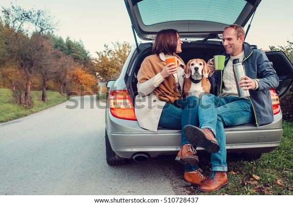 Tea party in car trunk - loving couple with dog\
sits in car trunk
