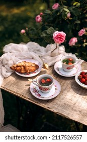 Tea Party From Vintage Cups With Saucer Top View. Herbal Tea With Fresh Strawberries. Tea Party Outdoors In The Rose Garden.