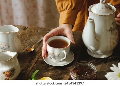 Tea party. Woman drinking tea during morning breakfast. Hand holding cup of black tea on wooden served table. - Powered by Shutterstock